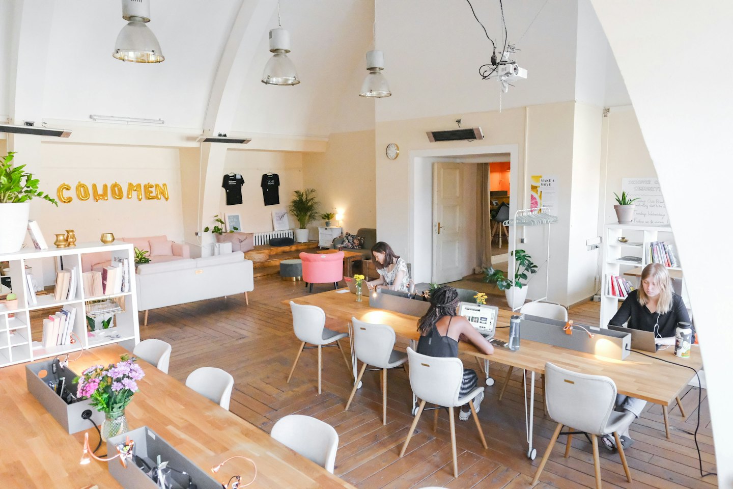 Persone che lavorano al computer su tavoli comuni in un luminoso spazio di co-working.